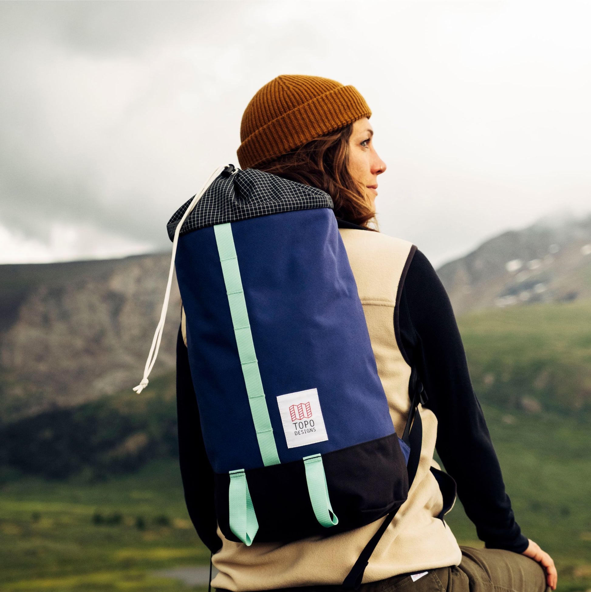 Navy and black backpack with mint green straps worn by person in mountains.
