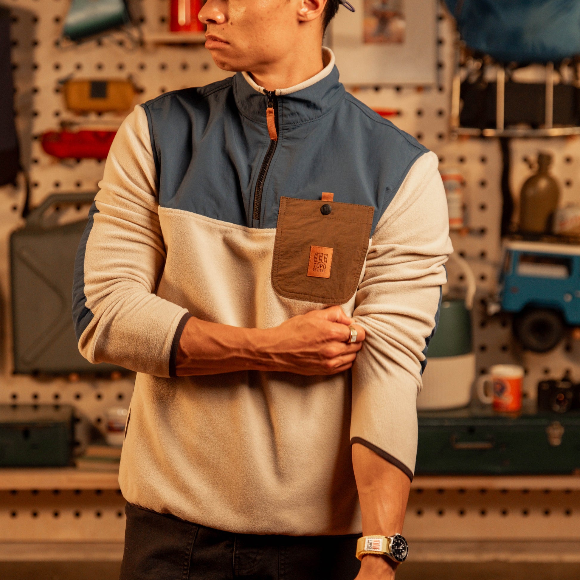 Men's fleece pullover with cream body, navy chest panel, brown pocket detail, and quarter-zip in garage setting.